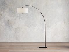 a floor lamp with a white shade on it in front of a concrete wall and wooden floor