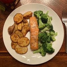 a white plate topped with potatoes and broccoli next to a piece of salmon