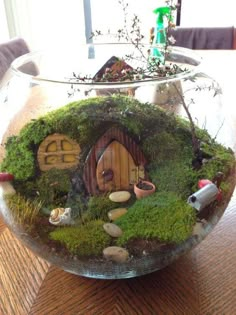 a glass bowl filled with green moss and small gnomes in it on top of a wooden table