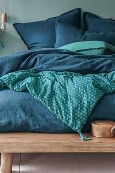 an unmade bed with blue sheets and green blankets on it, along with a wooden night stand