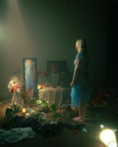 a woman standing in front of a mirror with flowers and candles on the floor next to it