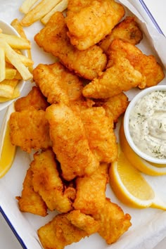 fried fish and french fries on a plate with lemon wedges, dip and sauce