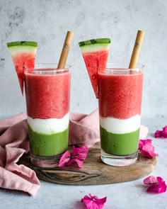 two glasses filled with watermelon and cucumber on top of a wooden board