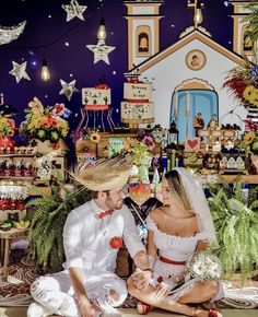 a man and woman sitting on the ground in front of a cake shop with decorations