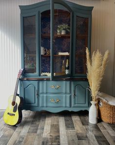 a blue china cabinet with a yellow guitar in front of it and a basket on the floor next to it