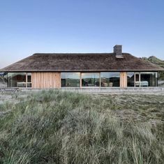 the house is surrounded by tall grass and has large windows that look out onto the ocean