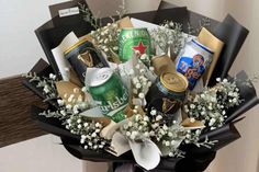 a bouquet of beer and snacks is wrapped in black paper with white baby's breath