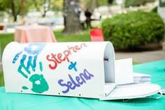 a mailbox with writing on it sitting on top of a blue tablecloth covered ground