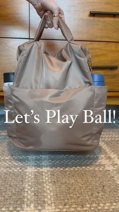 a person holding onto a gray bag with the words let's play ball on it