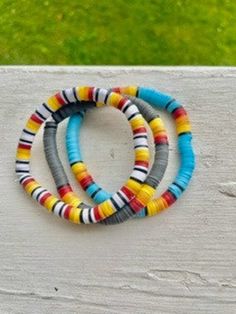 three bracelets are sitting on top of a piece of white wood with grass in the background