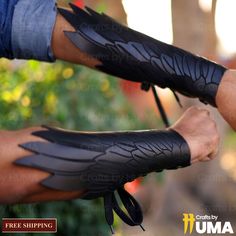 two hands with black leather gloves holding each other's wrist and palm, in front of trees