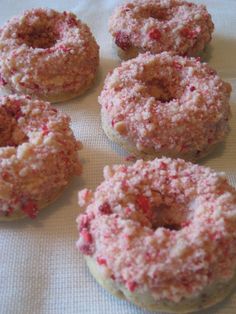 four doughnuts with pink sprinkles are on a white tablecloth