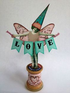 a paper doll is standing on top of a thread spool with the word love