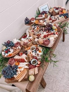 a wooden table topped with lots of cheese and crackers next to a white wall