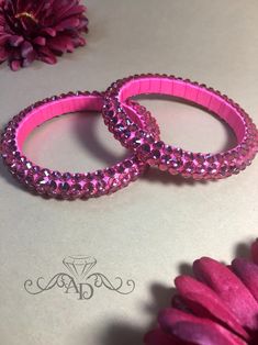 two pink bracelets sitting on top of a table next to a purple daisy flower