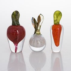 three glass vases with vegetables in them on a white surface, one is red and the other is green