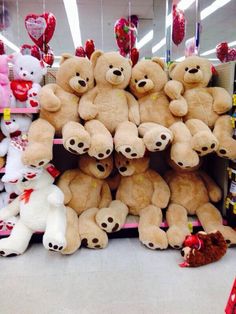 a bunch of teddy bears are stacked on top of each other in a store with hearts hanging from the ceiling