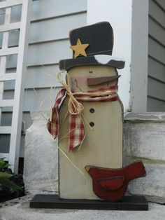 a wooden snowman with a hat and scarf on it's head sitting in front of a house