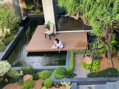 a person sitting on a wooden deck next to a small pond in front of a house