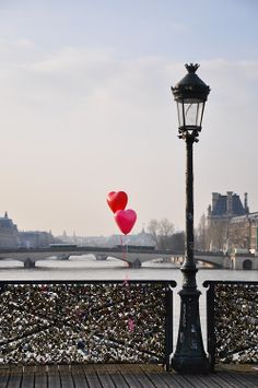 two heart shaped balloons floating in the air next to a lamp post on a bridge