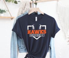 a t - shirt with the words hawks baseball on it hangs next to a denim jacket