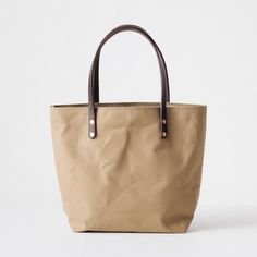 The Field Tan Canvas tote is a canvas and leather tote handmade in the KMM & Co. studio in Atlanta. Each one is meticulously crafted from heavyweight canvas and gorgeous full-grain leather. Field Tan Canvas is a type of cotton canvas known as duck cloth. It's one of the most durable types of cloth, and it's structured enough to stand up on its own. The Field Tan Canvas tote comes standard with Dark Brown handles. Classic Canvas Tote Bag For Everyday, Classic Everyday Canvas Tote Bag, Classic Everyday Waxed Canvas Bag, Classic Canvas Bag With Leather Handles, Classic Canvas Bag With Leather Handles For Everyday, Classic Leather Canvas Bag For Everyday, Classic Coated Canvas Bag For Daily Use, Classic Coated Canvas Tote Bag, Classic Canvas Bag For Everyday Use