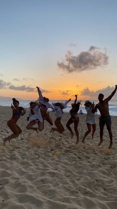 a group of people jumping in the air on top of a sandy beach at sunset