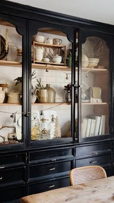 a black china cabinet with glass doors and shelves filled with dishes on top of it