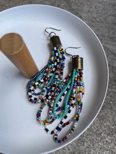 two pairs of beaded earrings on a plate next to a wooden spoon and pepper shaker