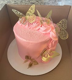 a pink cake decorated with butterflies and flowers in a box on top of a counter