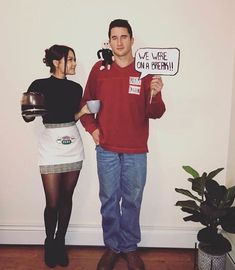 a man and woman standing next to each other in front of a wall holding signs