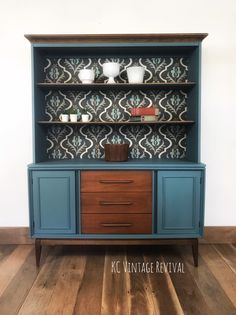 an old china cabinet painted in blue and brown with decorative wallpaper on the back