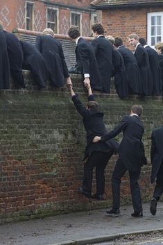 a group of men in suits climbing up the side of a brick wall with their arms raised