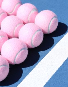 several pink tennis balls are lined up on a blue and white striped surface with one ball in the middle