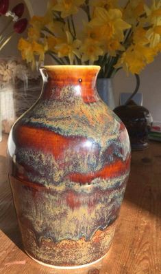 a vase sitting on top of a wooden table next to yellow daffodils