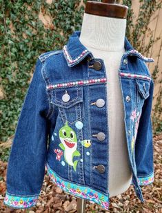 This Baby Shark Denim Jacket is perfect for your little one! Constructed from lightweight denim and detailed with Baby Shark characters, it makes a fun and stylish addition to any wardrobe. With its added ribbon detail, it's sure to be a hit with the little ones. These jackets run TRUE TO SIZE. Please note that jackets are personalized and made to order. They will not always be exact replicas. Denim color may vary. Baby Shark Characters, Shark Jacket, Remake Clothes, Custom Jean, Custom Jean Jacket, Lightweight Denim Jacket, Custom Barbie, Girls Denim Jacket, I Love My Daughter