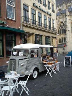 an old van is parked in front of a building with tables and chairs around it