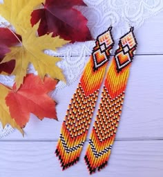 two pairs of beaded earrings sitting on top of a table next to autumn leaves