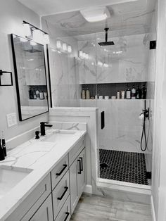 a white bathroom with marble counter tops and black accents on the shower wall, along with two sinks