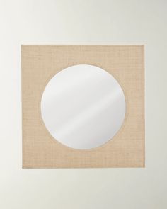 a white round mirror sitting on top of a beige cloth covered wall next to a window