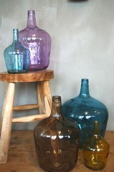 three different colored glass bottles sitting on top of a wooden stool