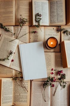 an open book sitting on top of a table next to some flowers and a candle