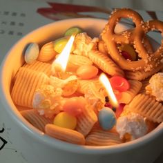 a bowl filled with candy and pretzels next to a lit candle