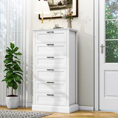 a white chest of drawers sitting next to a potted plant in a living room