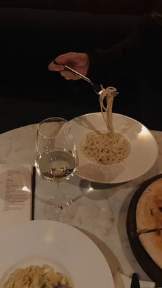 a person is eating pasta at a table with wine glasses and silverware on it