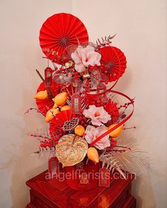 an arrangement of flowers and red umbrellas on top of a wooden box in front of a white wall