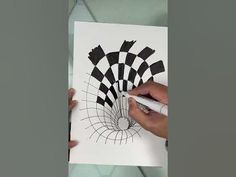 two hands are drawing on a piece of paper with black and white squares in the background