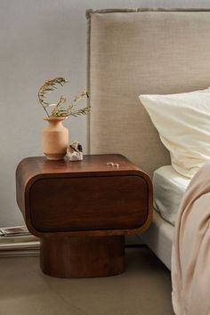 a bed sitting next to a nightstand with a plant on it