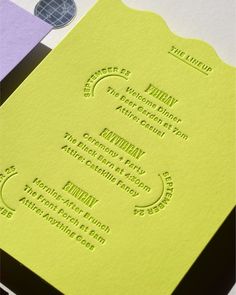 a yellow and green wedding card on top of purple and white paper with black lettering