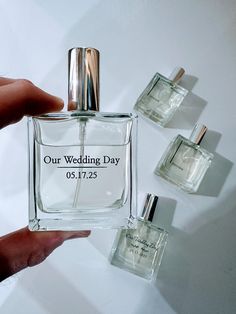 a hand holding a small bottle of perfume next to three smaller bottles on a white surface